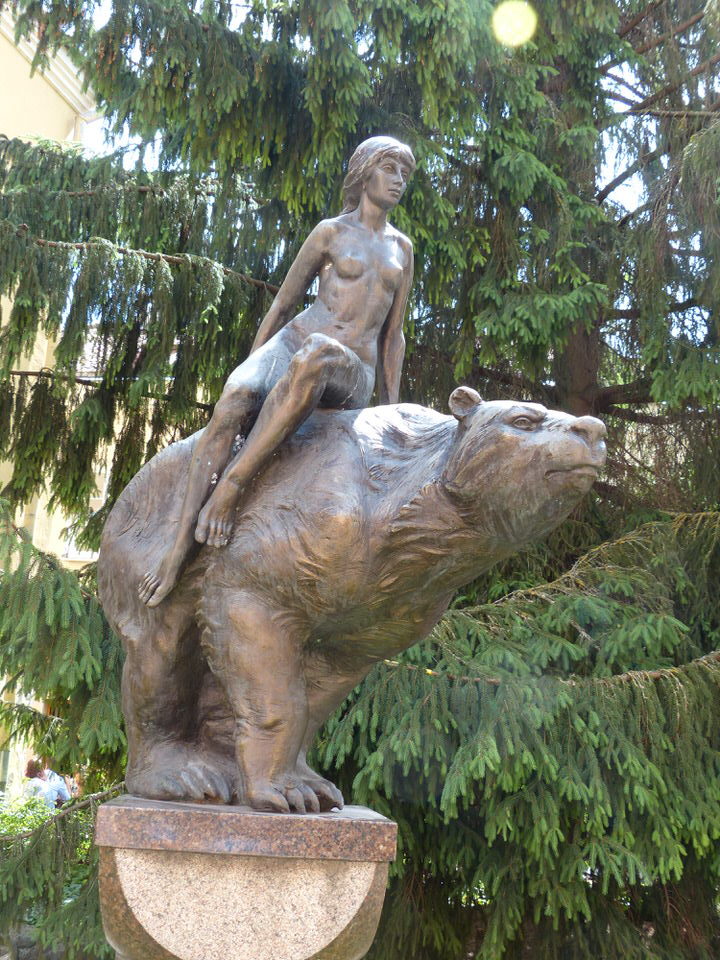 a bronze statue of a naked woman sat on top of a bear